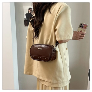 Close-up of brown leather crossbody bag featuring metal studs and adjustable strap