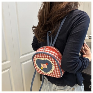 Detail of red checkered mini backpack featuring denim heart and lace trim on a model