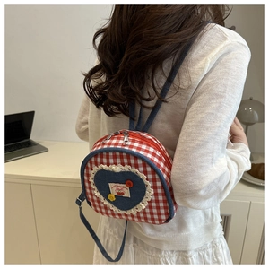 Detail of red checkered backpack featuring blue denim heart pocket with white lace trim