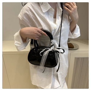 Close-up of black glossy shell bag with white lace bow and detachable strap details