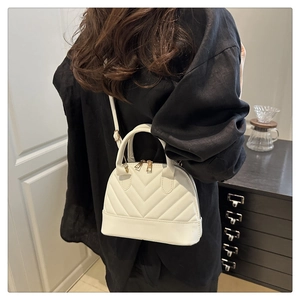Detailed view of white quilted leather shell bag with gold hardware on a model