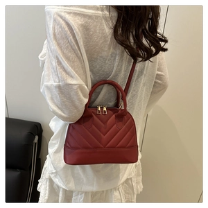 Detail view of deep red quilted shell bag worn by model showing dual handles and gold zipper
