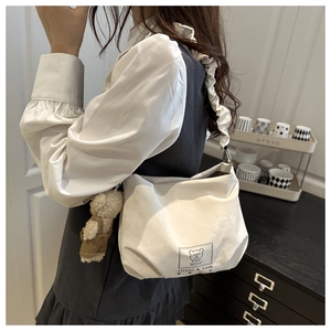 Detail of white leather crossbody bag with ruffled strap and plush bear charm