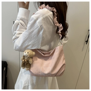 Pink crescent shoulder bag with ruffle strap and teddy bear pendant worn by model