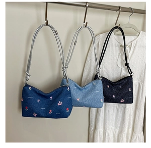 Close-up of three denim shoulder bags with floral embroidery and chain straps