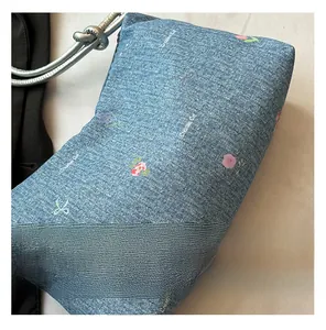 Close-up of light blue denim tote bag with floral prints and silver rope handle detail