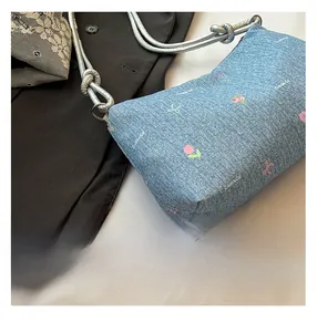 Detail of light blue denim tote with colorful floral embroidery and silver woven rope strap