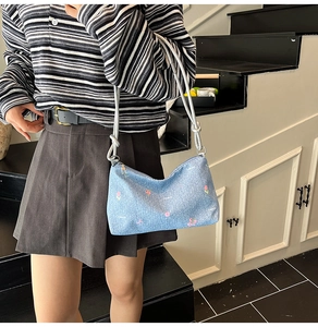 Detail of light blue denim tote bag with pink floral embroidery and knot strap on a model