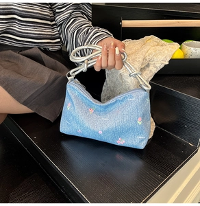 Detail of light blue denim tote bag with pink floral embroidery and silver rope handle