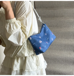 Close-up of blue denim tote bag with pink floral embroidery and silver metal hardware