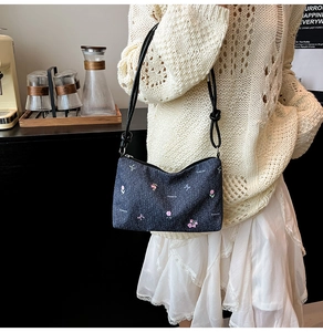 Detail view of denim tote bag with tulip embroidery and black leather strap on a model
