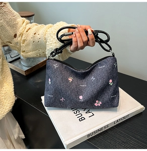 Detail of embroidered floral patterns and brand printing on dark blue denim handbag