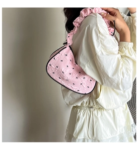 Detailed texture of pink ballet-style shoulder bag with black bow embroidery and ruffled strap