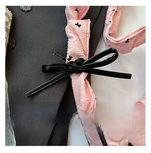 Detail of pink crepe texture fabric with black butterfly print and leather bow accent