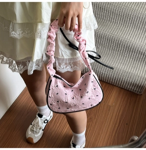 Detailed view of pink bow-print shoulder bag with textured fabric and ruffled strap