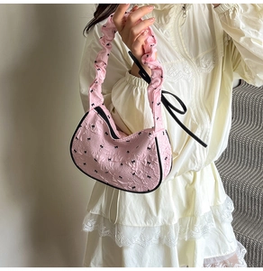 Detail of pink hobo bag with black bow prints and ruffled strap on model