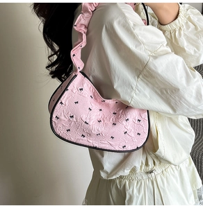 Detail of pink pleated underarm bag with black bow embroidery and ruffled shoulder strap