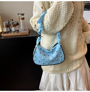 Detail of light blue pleated hobo bag with bow embroidery and ruffled shoulder strap