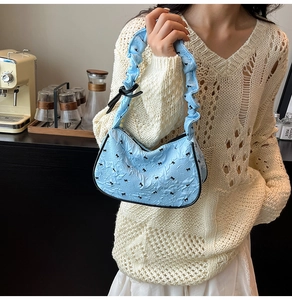 Detail of light blue pleated handbag with black bow patterns and ribbon handle