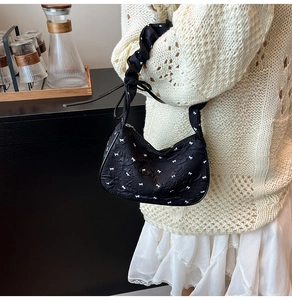 Detail of black underarm bag featuring white bow prints and gathered ruffle shoulder strap