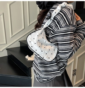Detail of white textured underarm bag with black bow patterns and elegant shoulder strap