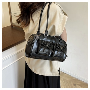 Close-up of black glossy shoulder bag with bow details and functional double front pockets