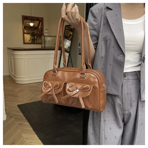 Close-up of caramel brown glossy leather bag with bow details and twin pockets
