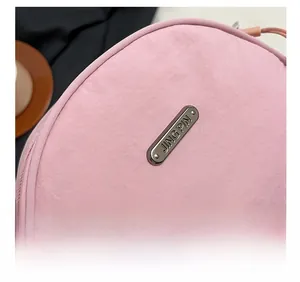 Detail of pink fabric shell bag featuring a polished oval metal brand plaque logo