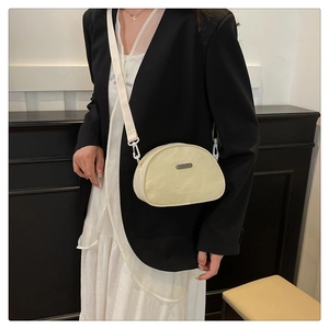 Detail of a cream nylon dumpling bag with a metal brand plate on a model's shoulder