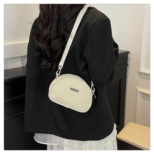 Detailed side view of a cream oxford fabric shell crossbody bag on a model