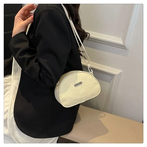 Detail of a creamy white crescent crossbody bag on a model wearing a black blazer