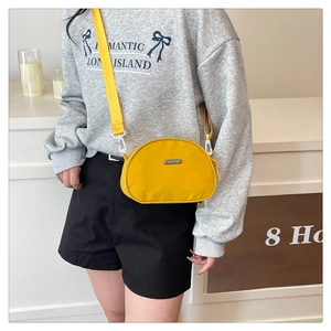 Detailed close-up of a bright yellow nylon crossbody bag featuring a metal logo and wide strap
