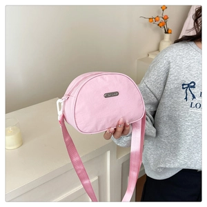 Detail of light pink nylon crossbody bag showing the silver metal logo plate and strap