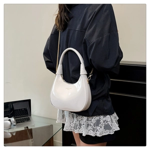 Close-up of white patent leather crescent bag with gold chain strap and metallic finish