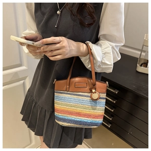 Detailed view of colorful woven straw bag featuring brown leather handles and gold pendant