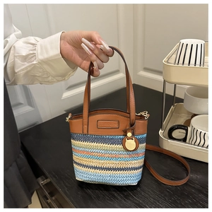 Détail du sac seau tissé coloré avec poignées en cuir marron et plaque métallique