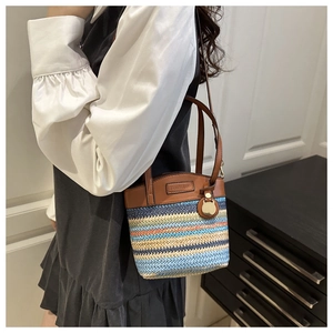 Detail of color-block woven bucket bag with brown leather handle and gold charm