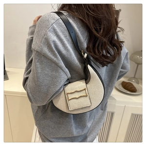 Gros plan du sac demi-lune en toile beige avec bordure en cuir noir et boucle dorée