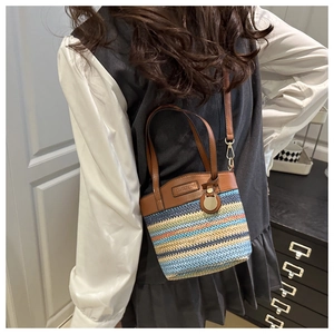 Détail du sac seau bicolore en paille tressée avec lanières et finitions en cuir brun