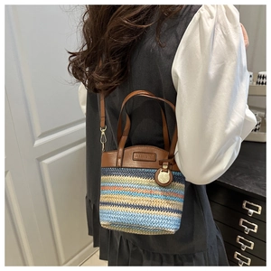 Détail du sac seau en paille bicolore avec poignées en cuir et garnitures dorées