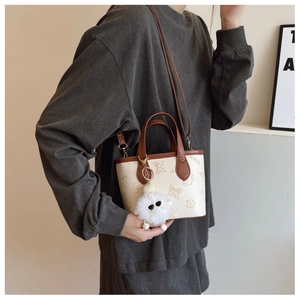 Detail of retro beige and brown crossbody bucket bag with cartoon prints and fur ball charm
