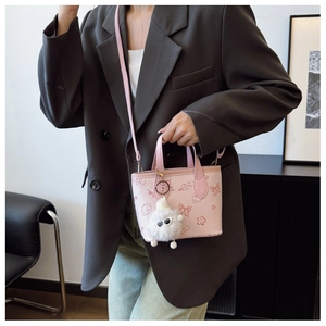Detail of light pink bucket bag with floral patterns and plush doll charm on shoulder