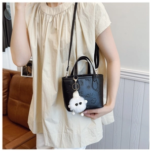 Detail of black embossed leather handbag with white fur pompom and metal hardware