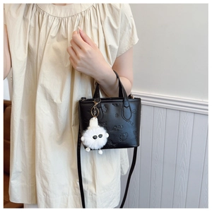 Detail of black embossed leather bucket bag with a white plush monster charm accessory