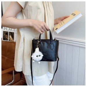 Detail of black embossed bucket bag featuring a white plush monster charm and fine texture