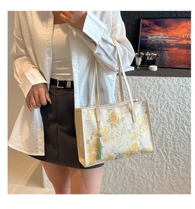 Detail of elegant beige tote bag with floral embroidery and silk tassel on a model