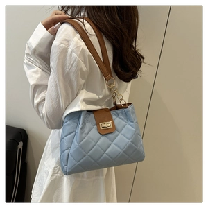 Détail du sac matelassé bleu clair avec rabat en cuir marron et fermoir doré rotatif
