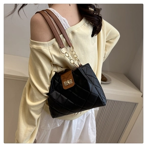 Detail of black quilted tote bag with brown leather flap and golden twist lock
