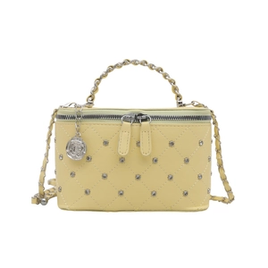 Petit sac matelassé jaune avec clous argentés et bandoulière chaîne sur fond blanc