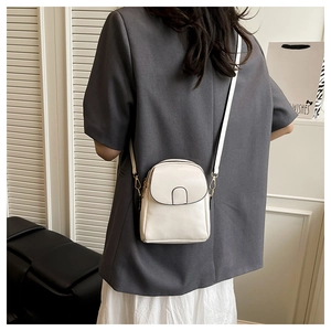 White mini crossbody flap bag with contrast piping and metal chain worn by a model